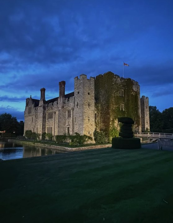 Hever Castle floodlit at dusk, its outline reflected in the moat
