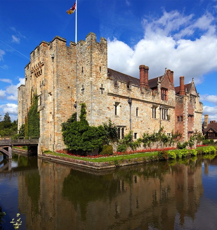 Hever Castle's stone range reflected in the still water of the moat, with roses along the bank