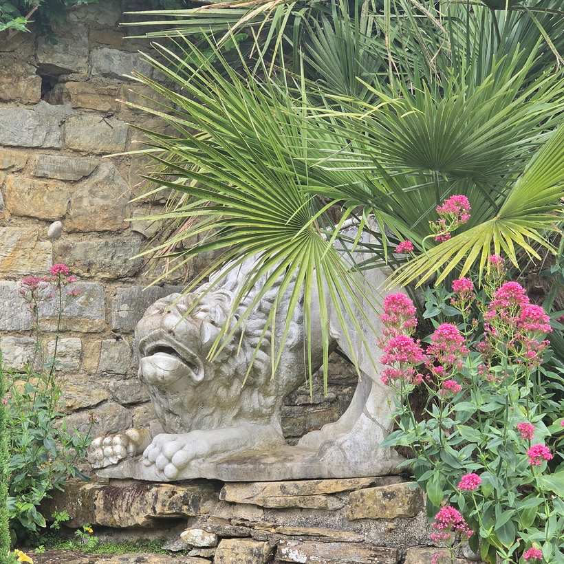 A carved stone lion set into a garden wall at Hever Castle, with red flowers around it